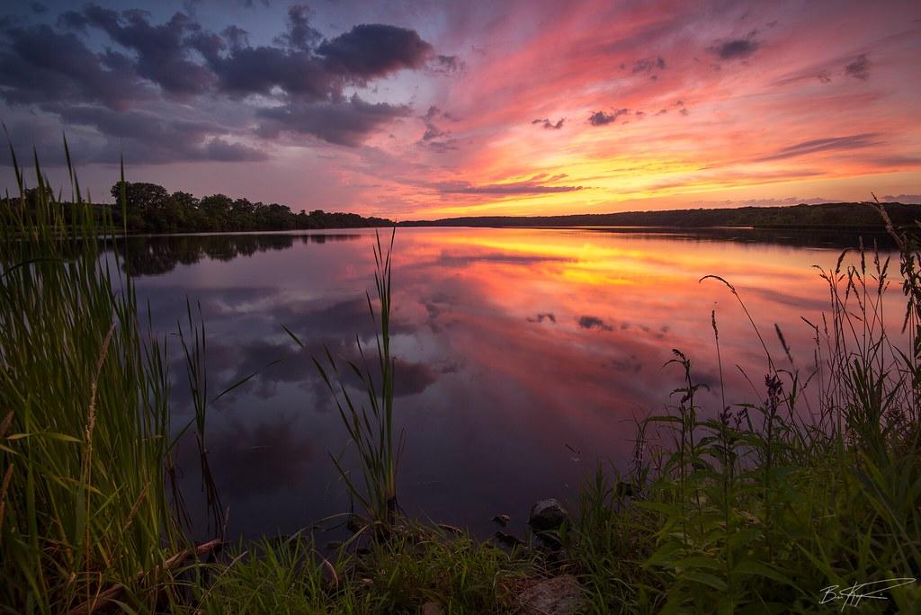 A vibrant sunset over a calm lake, reflecting colorful clouds and sky.