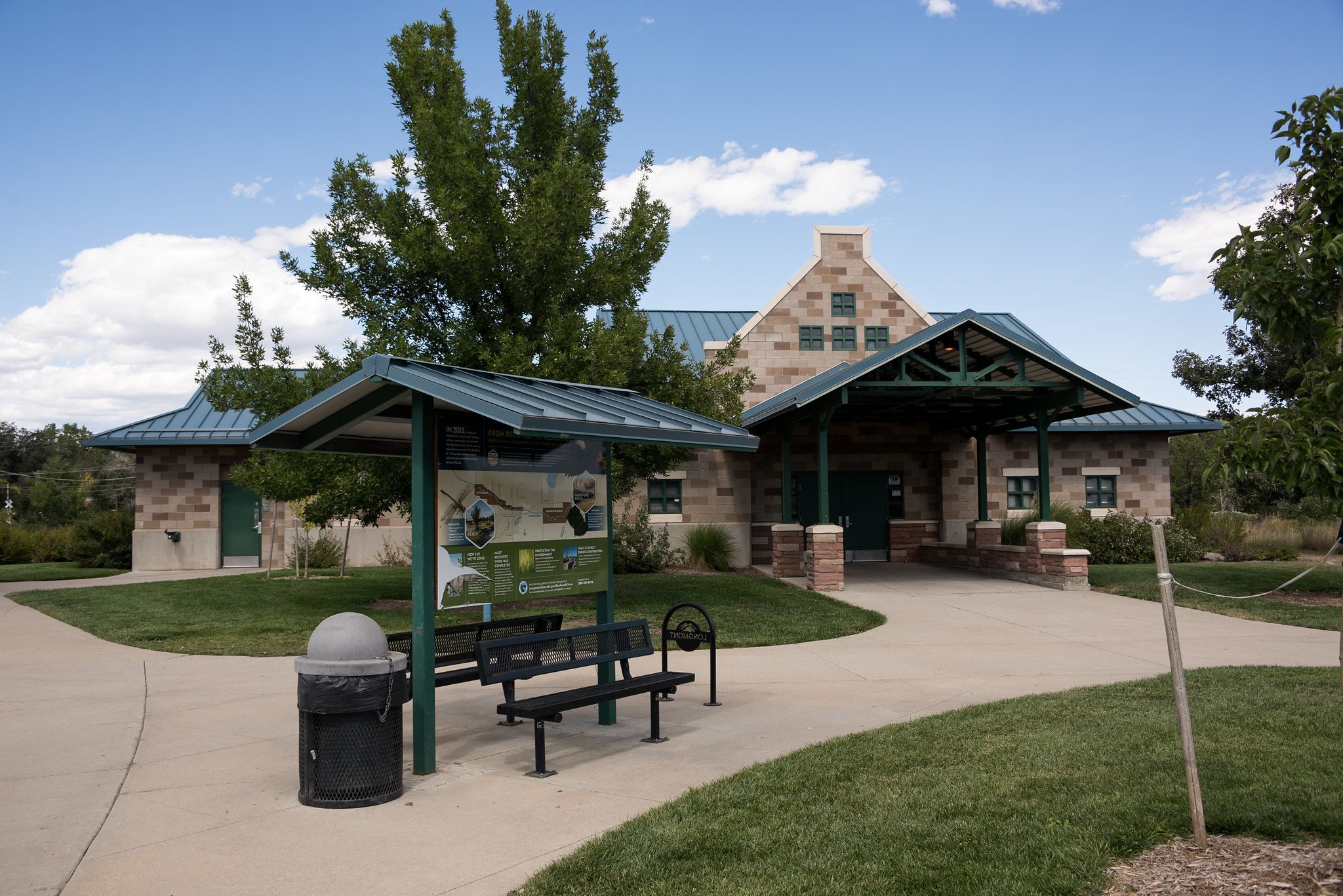 Stone building with green roof, information kiosk, and benches on a sunny day. - Longmont Loop - South