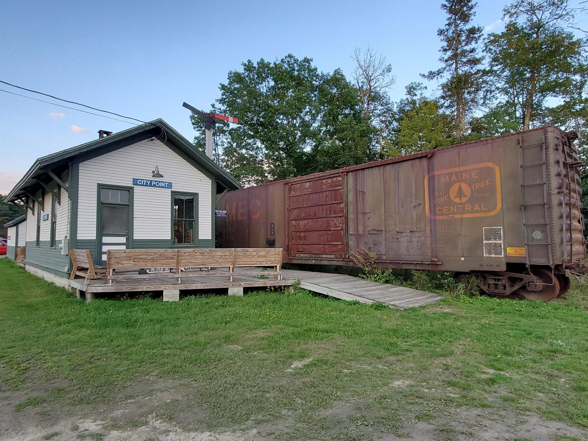 A small white building with a porch next to a rusty old train car.