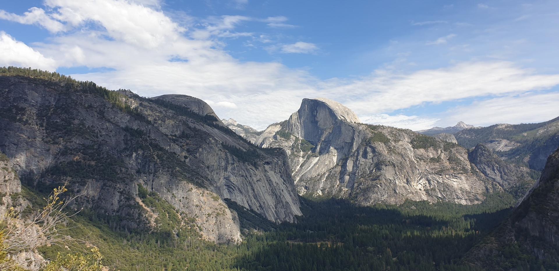Panoramic view of a vast mountainous valley under a partly cloudy sky.