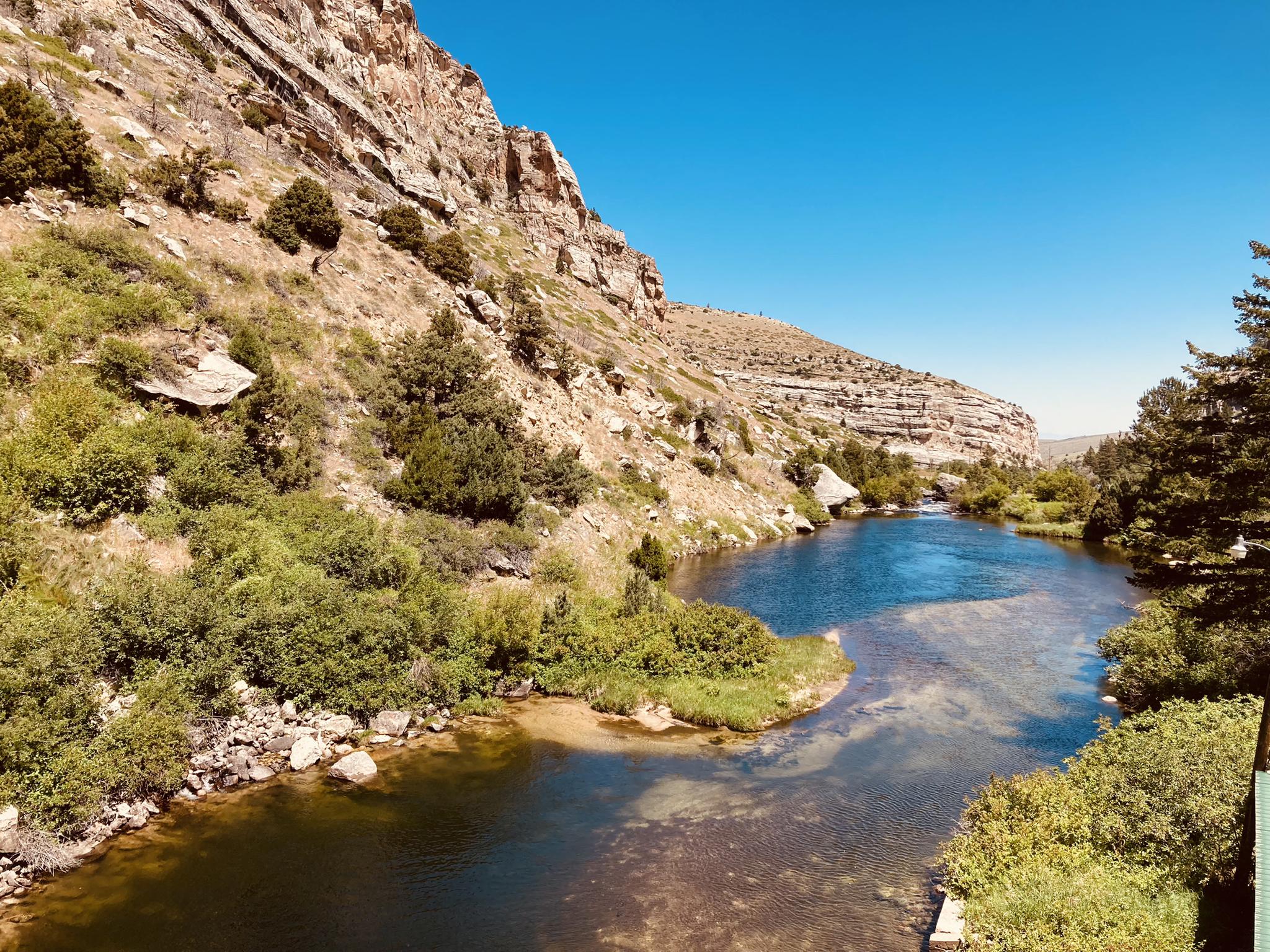 A serene river winds past steep, sunlit rocky cliffs and green foliage.