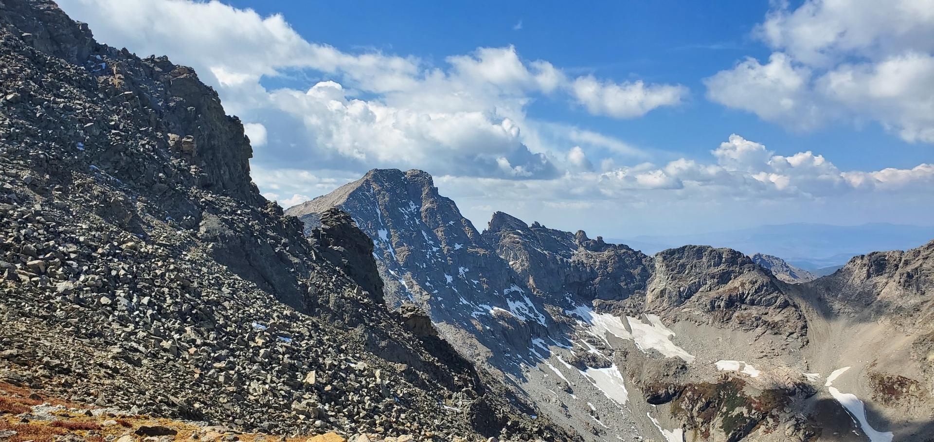 Rugged, rocky mountain peaks with snow patches under a bright, cloudy sky.