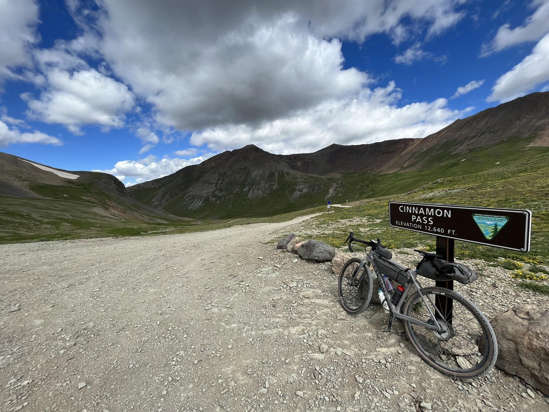 Bicycle parked next to a sign on a gravel road in a mountain pass.