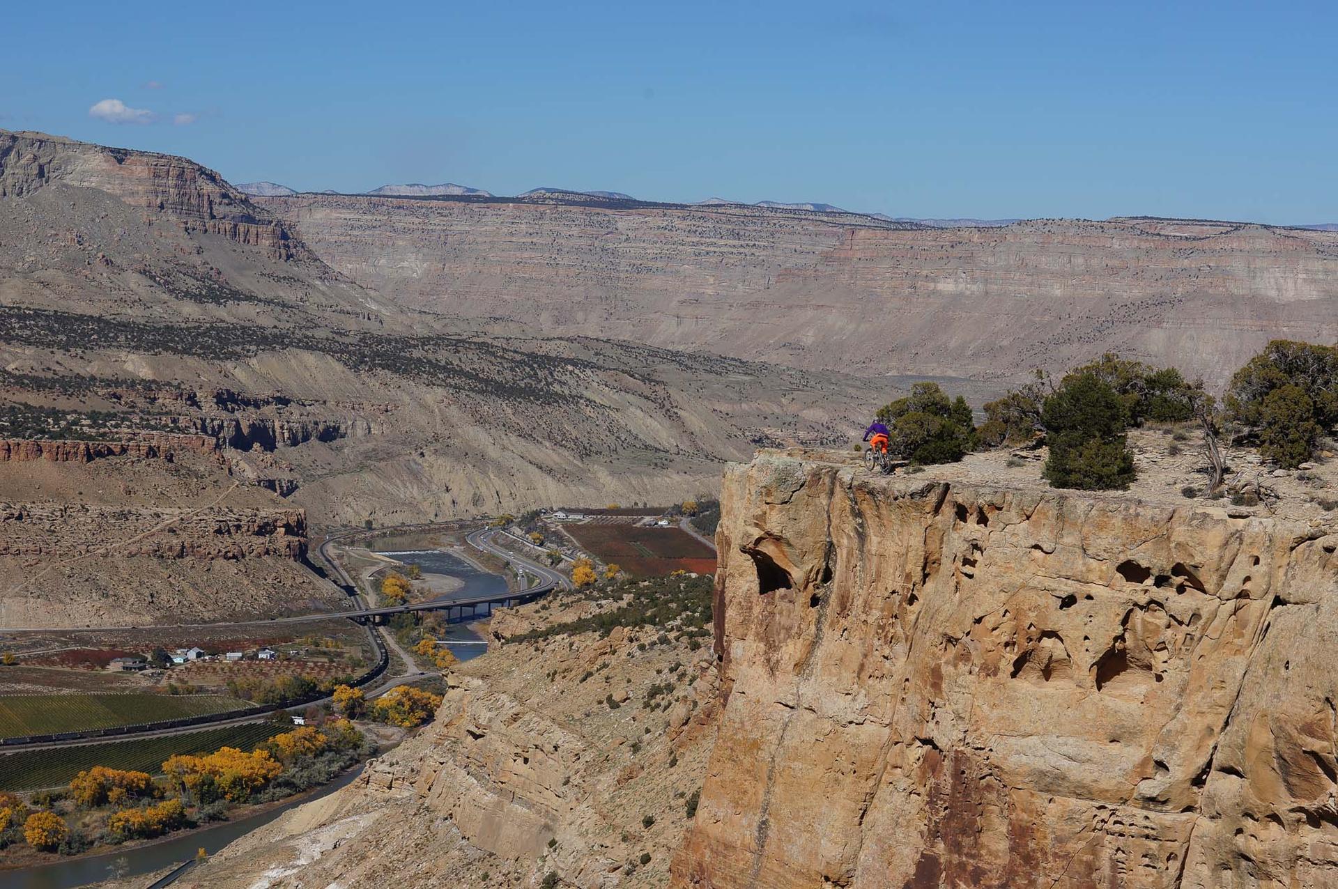 Sunny view of a person on a cliff overlooking a river valley and fields.
