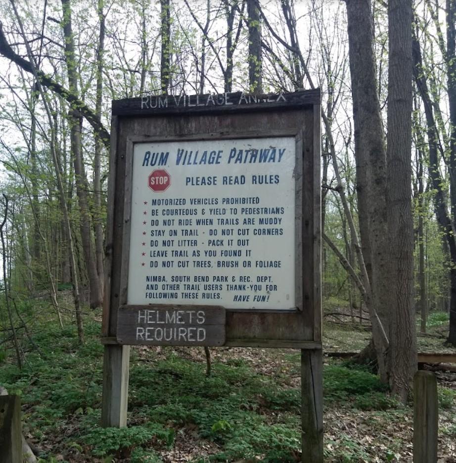A wooden sign detailing pathway rules stands in a lush, green forest.