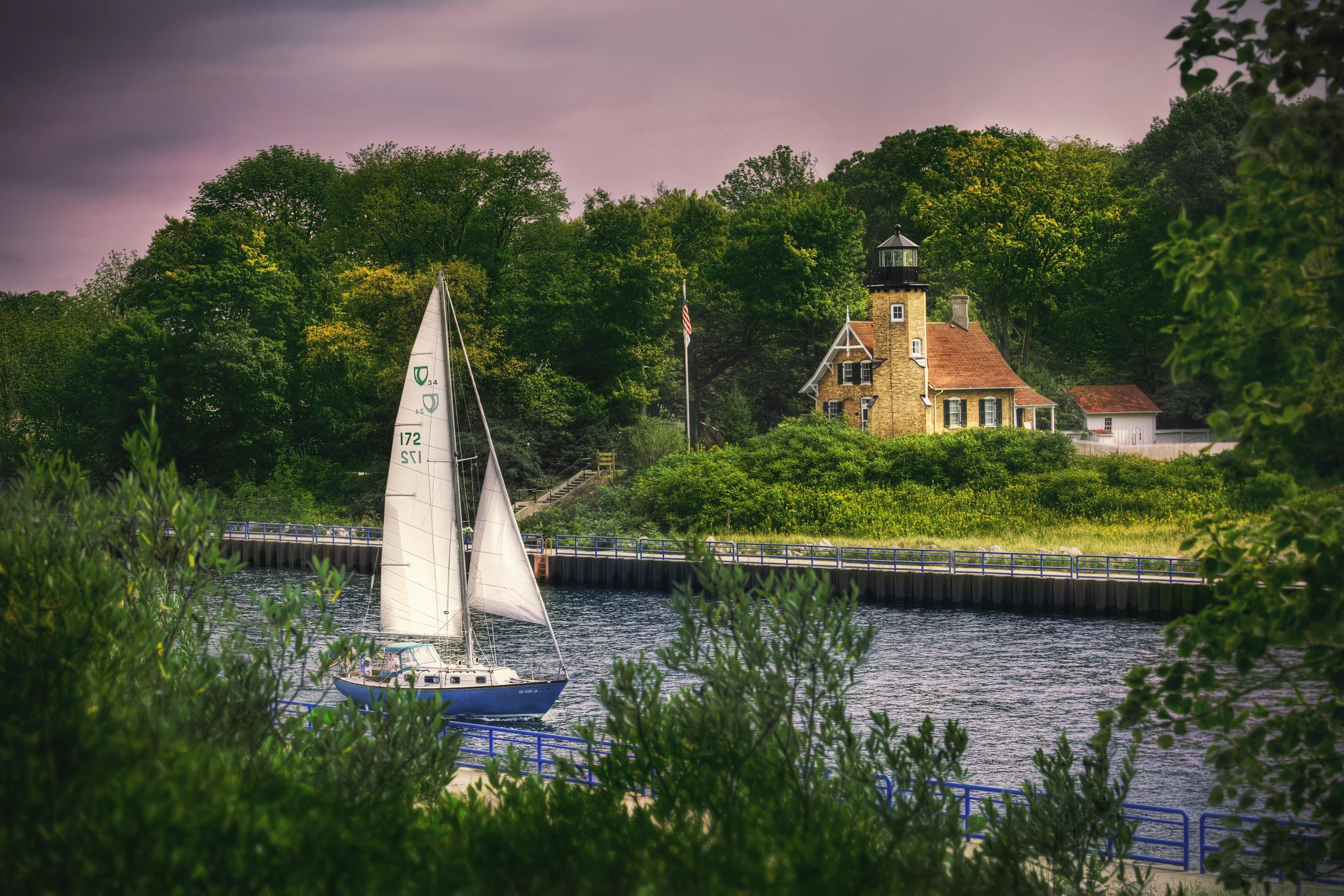 A sailboat glides on a waterway near a historic building with a tower.