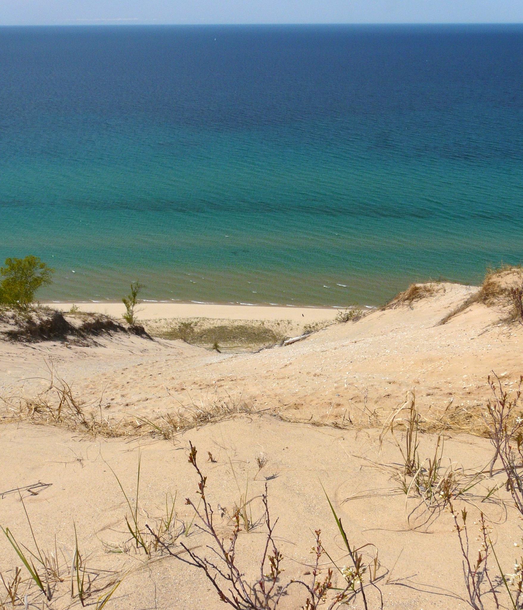 Sandy dune overlooking a beach and vast blue-green water on a sunny day.