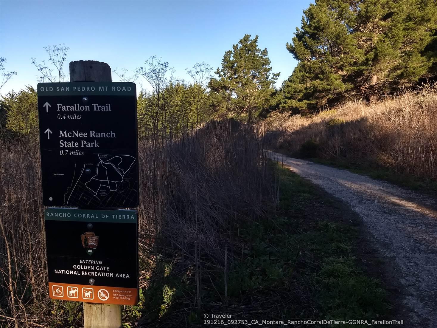 Trail sign with directions next to a dirt path, surrounded by dry brush.