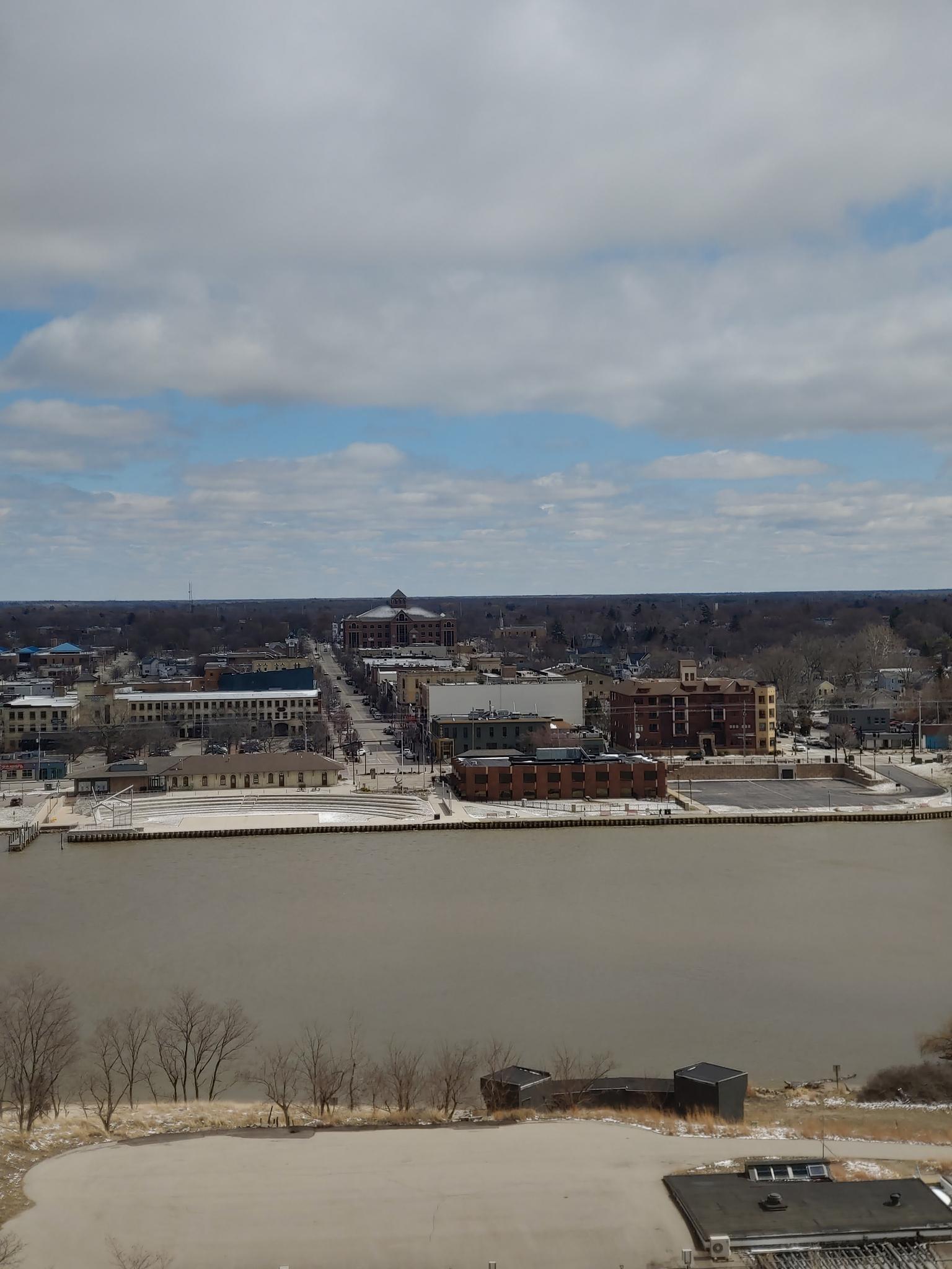 Aerial view of a town across a wide river with snowy banks under a cloudy sky.