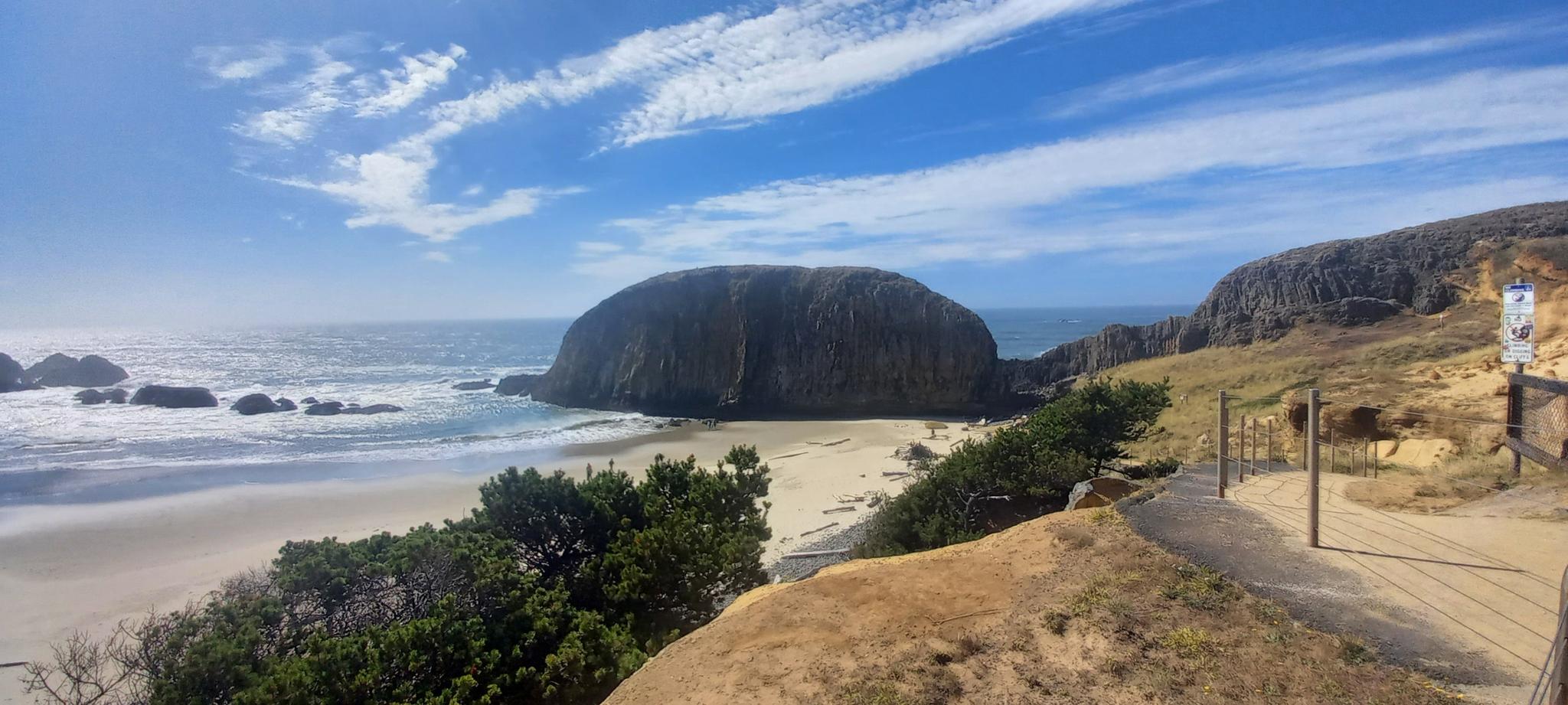 Panoramic view of a large rock on a sandy beach with ocean waves.