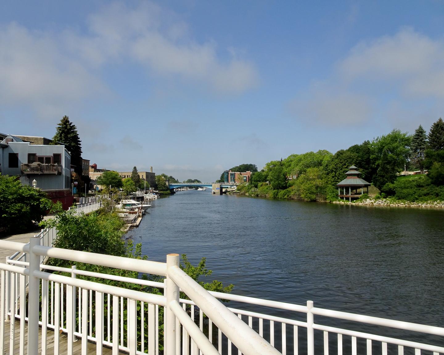 Wide river flowing through an urban area with green trees on a sunny day.