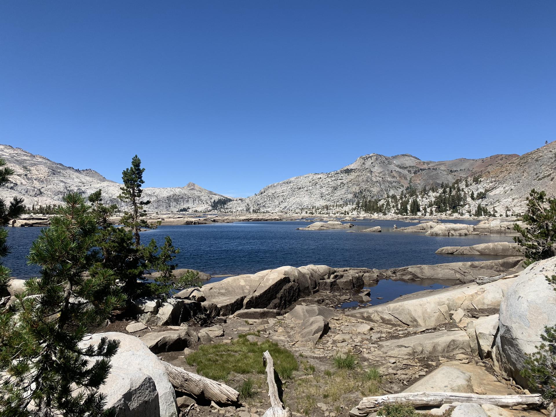 Sunny day over a clear blue lake surrounded by rocky mountains and sparse trees.