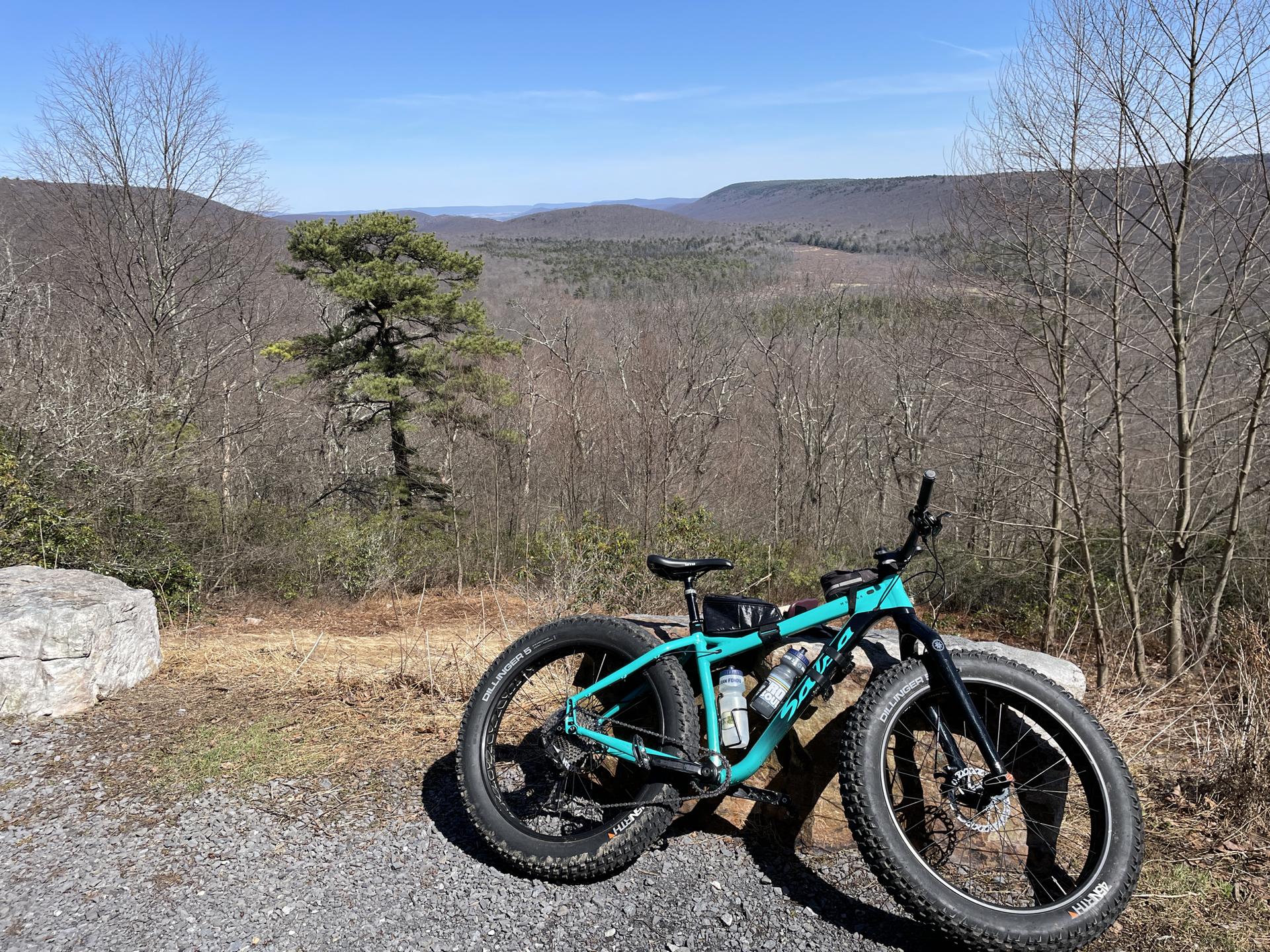 Teal fat-tire bike parked at a scenic mountain overlook on a sunny day.