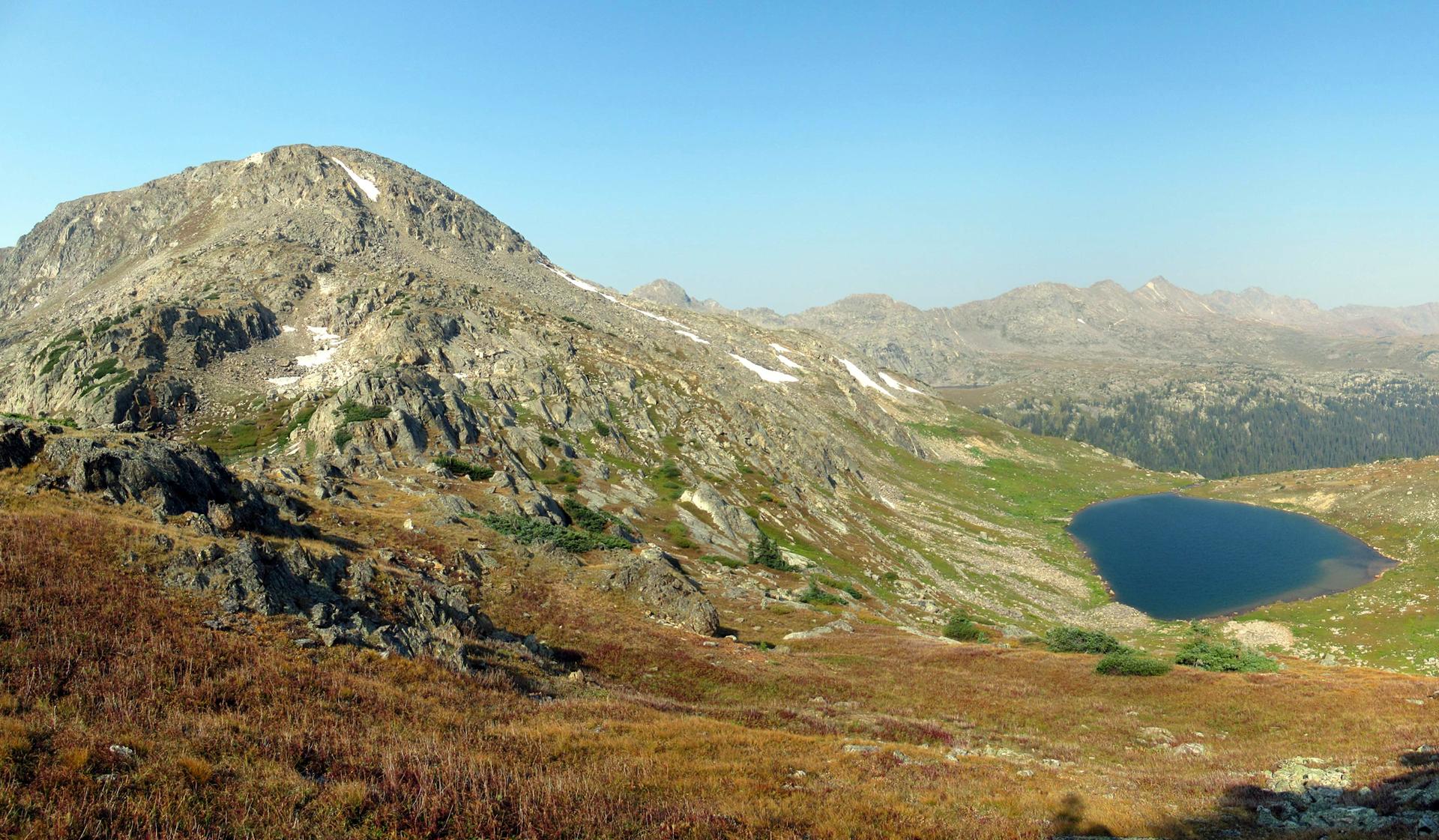 Panoramic view of a mountain, a deep blue lake, and a vast landscape.