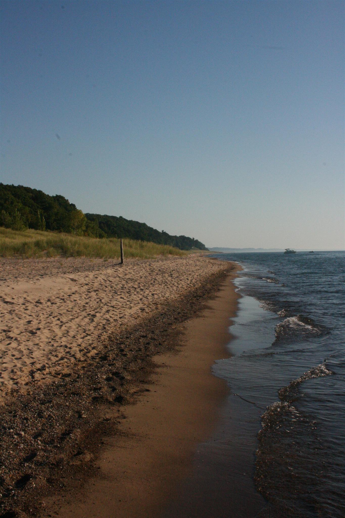 A long sandy beach meets calm water under a clear blue sky.