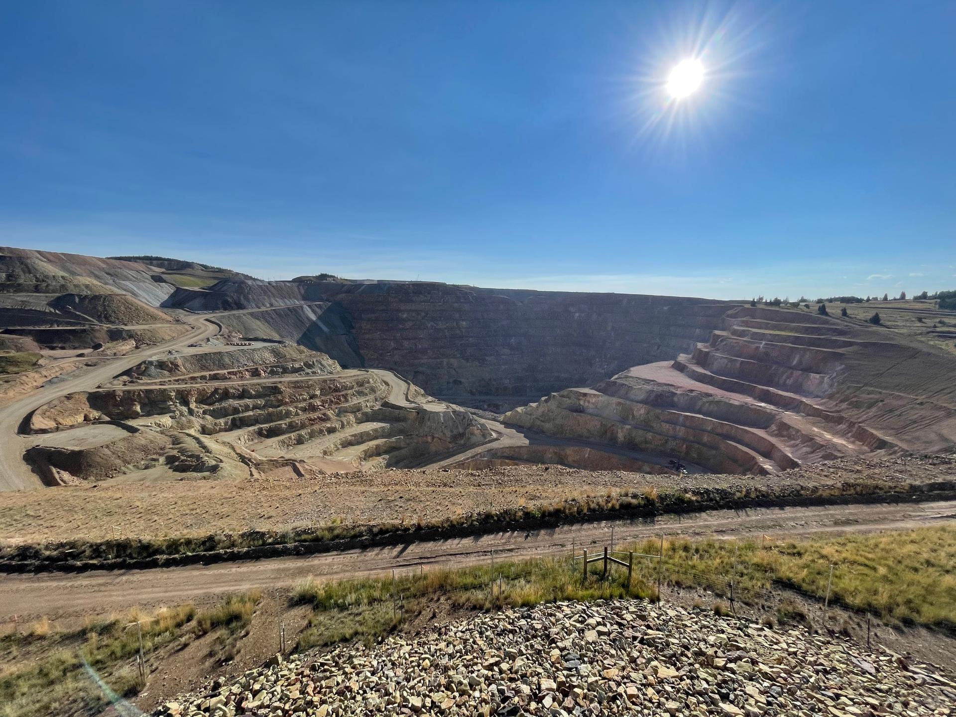 A vast open-pit mine with terraced walls under a bright sunny sky.