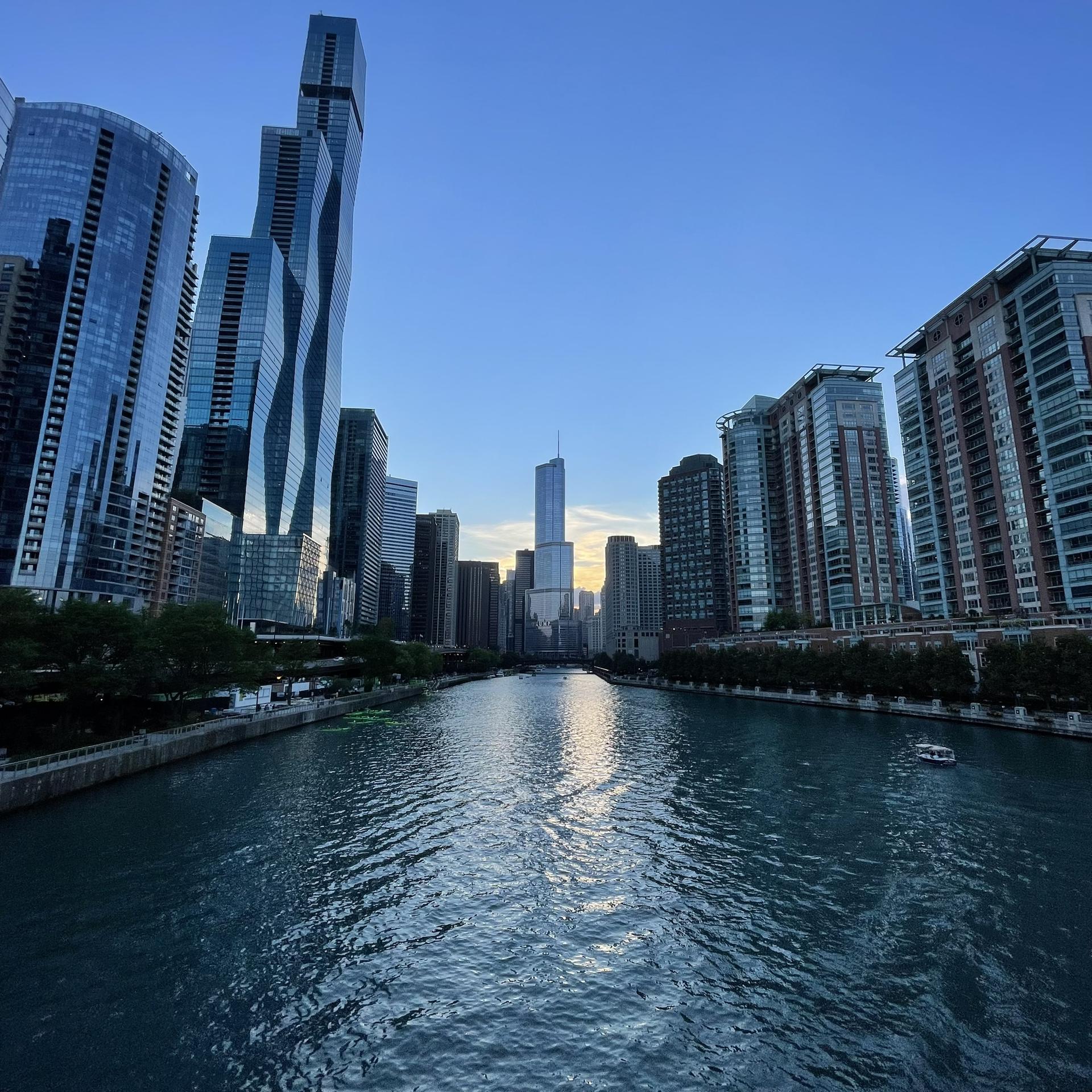 A river flows through a city skyline at dusk with a small boat.