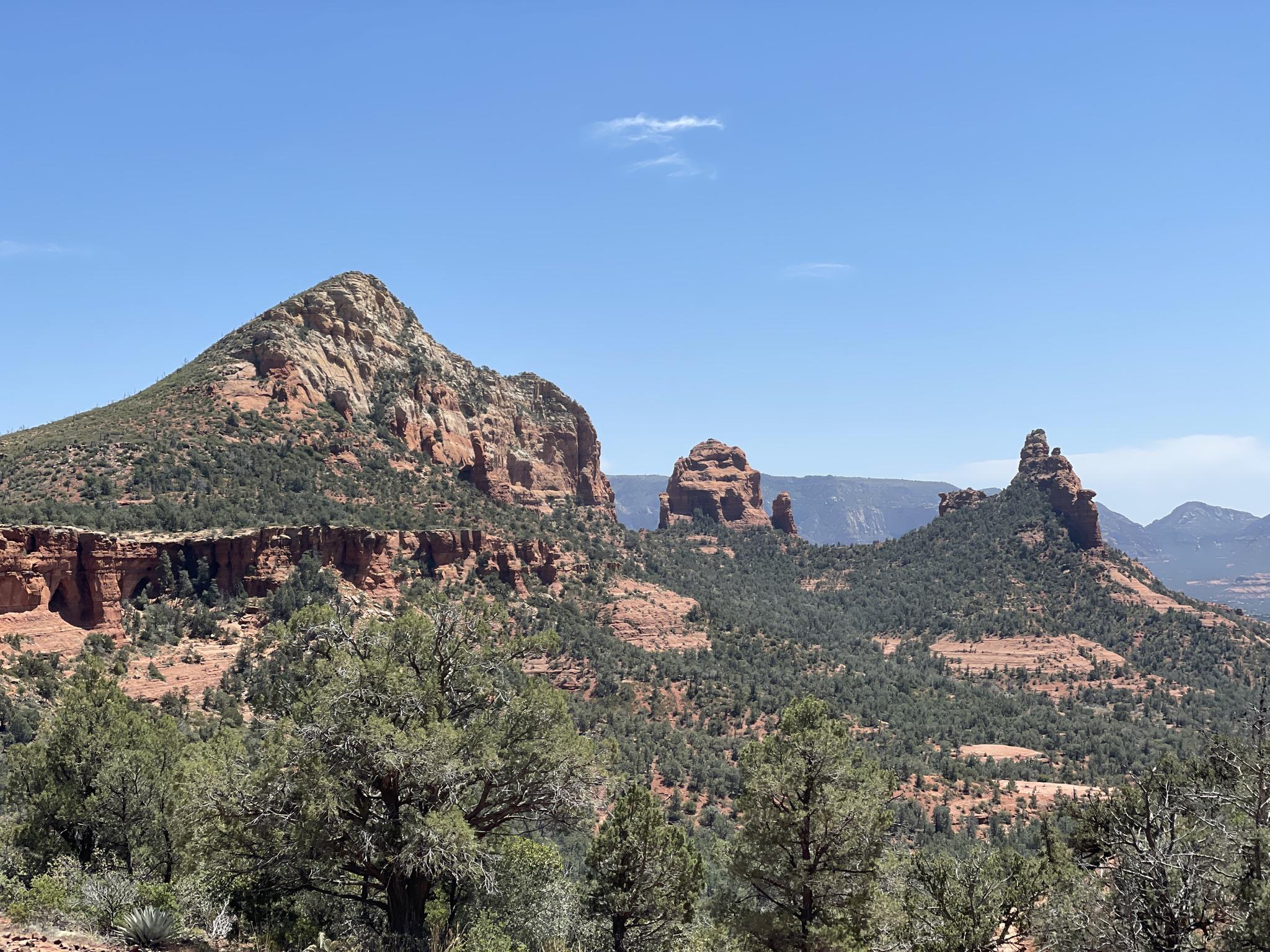Distant red rock peaks and green forested hills under a bright sky.