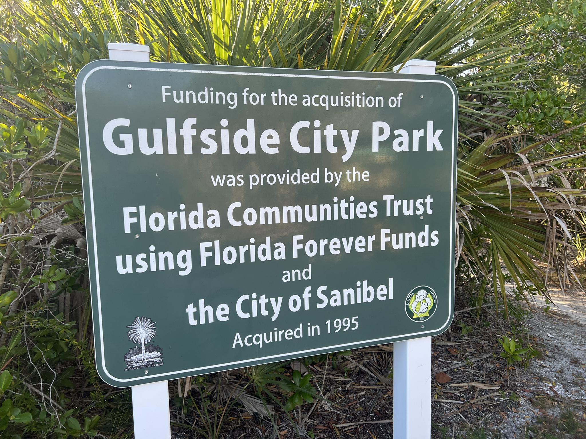 Green sign with white text, surrounded by green bushes.