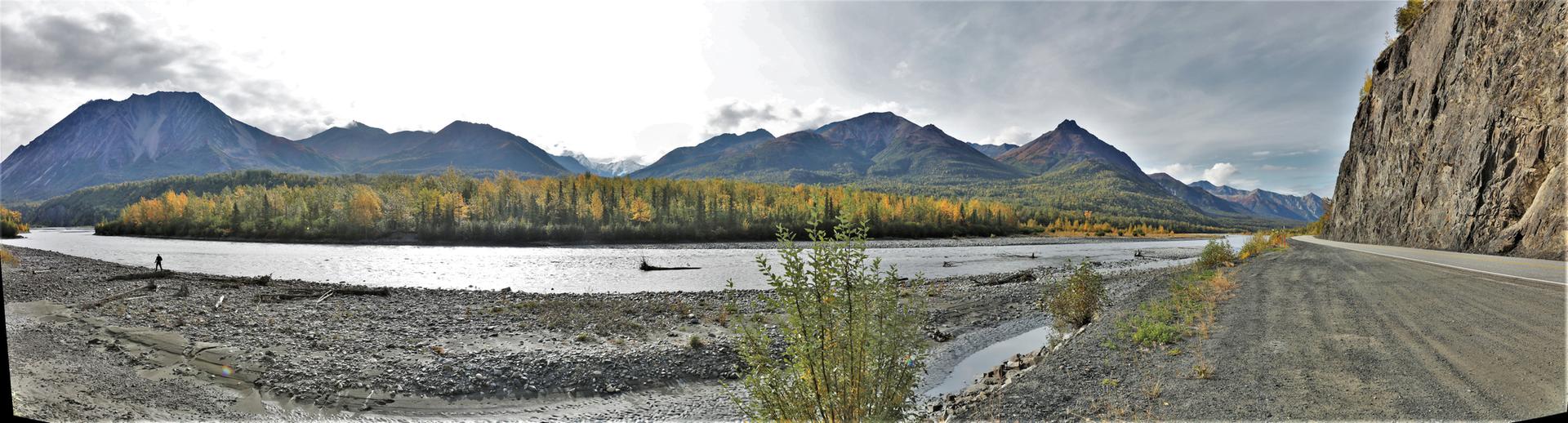 Panoramic view of a wide river, autumn trees, and mountains under an overcast sky.