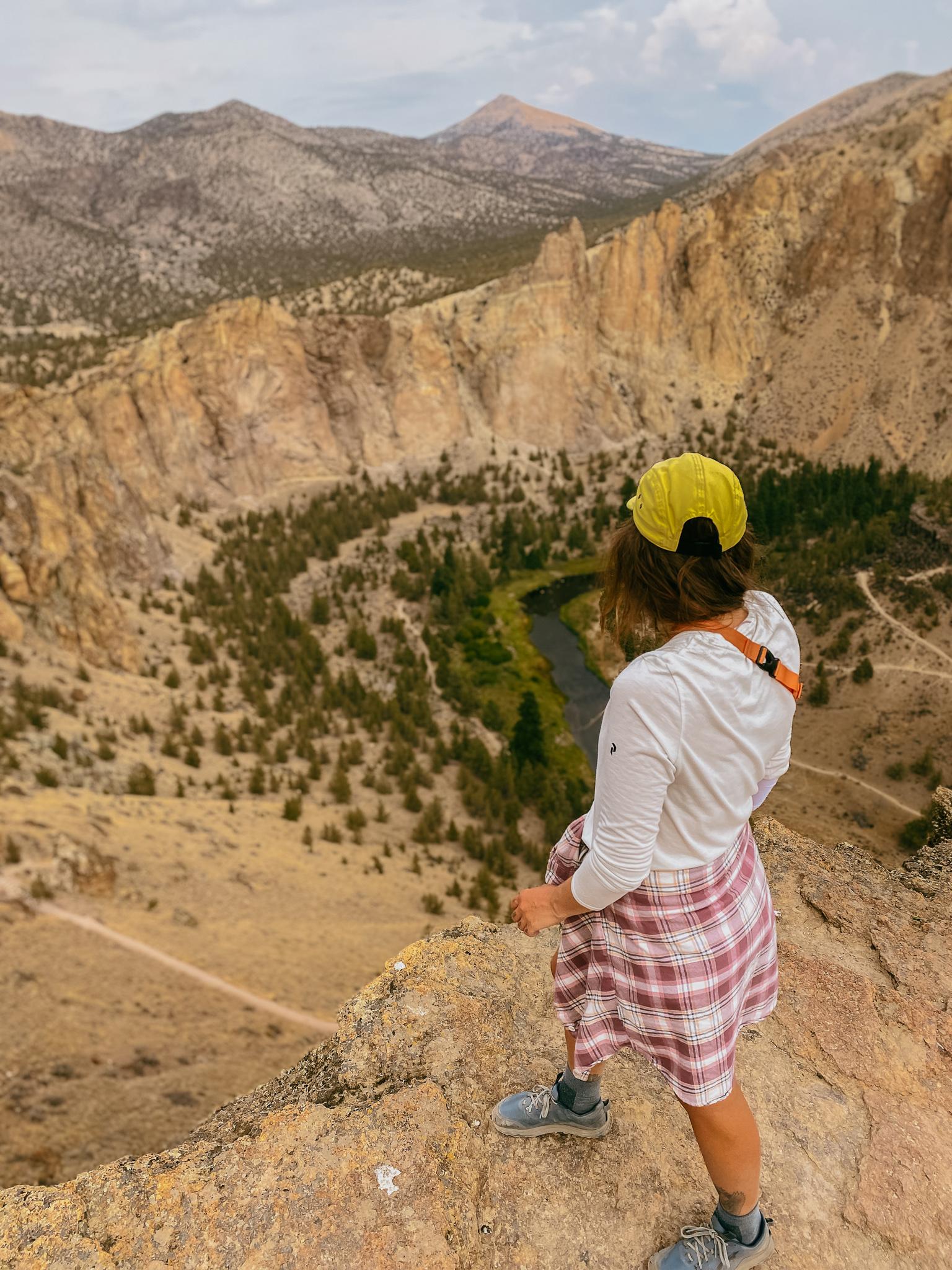 Hiker on a cliff edge overlooking a deep canyon with a winding river.