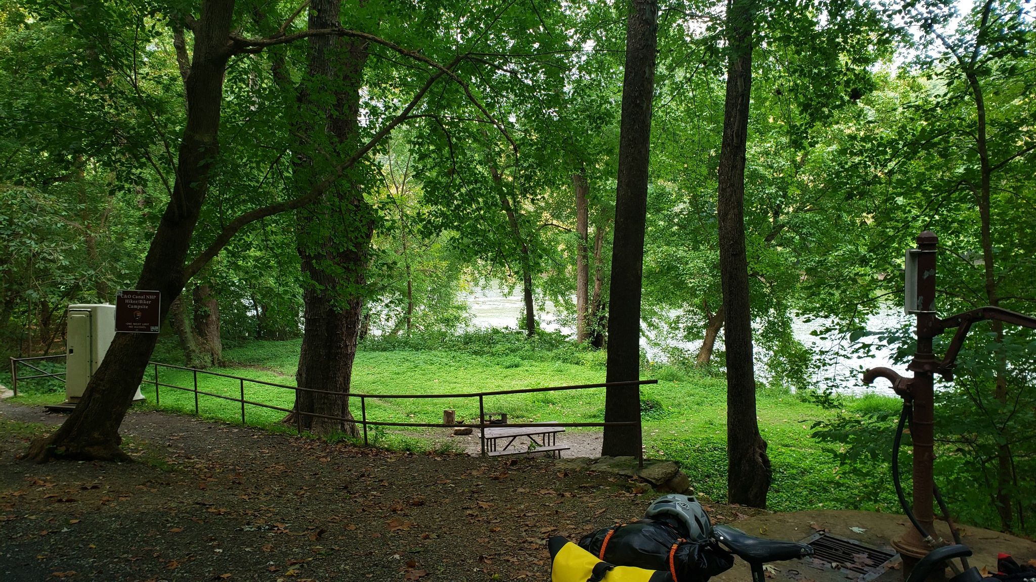 Bicycle parked in a shaded, green forest clearing next to a river. - Horseshoe Bend campsite loop from Shepherdstown
