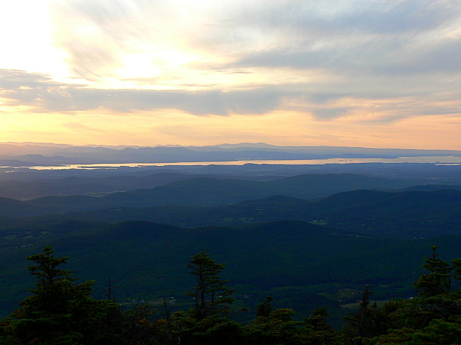 Vast mountain range and distant water under a colorful sunset sky.