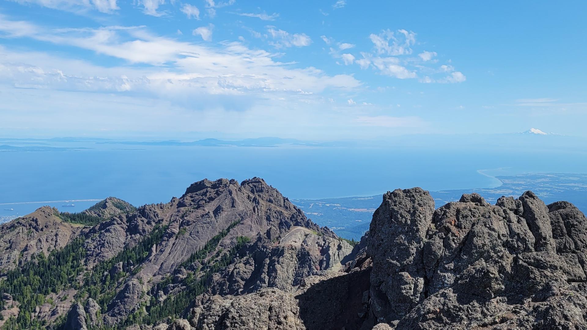 Jagged mountain peaks rise above a vast blue ocean under a clear sky.
