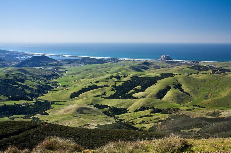 Sunny panoramic view of green rolling hills meeting a vast blue ocean.