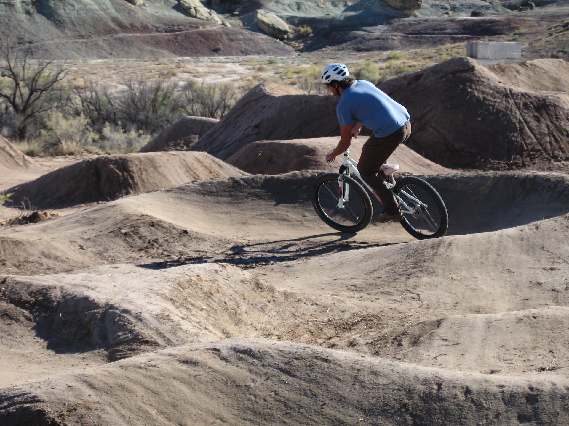 Mountain biker riding on a dirt pump track with sculpted mounds.