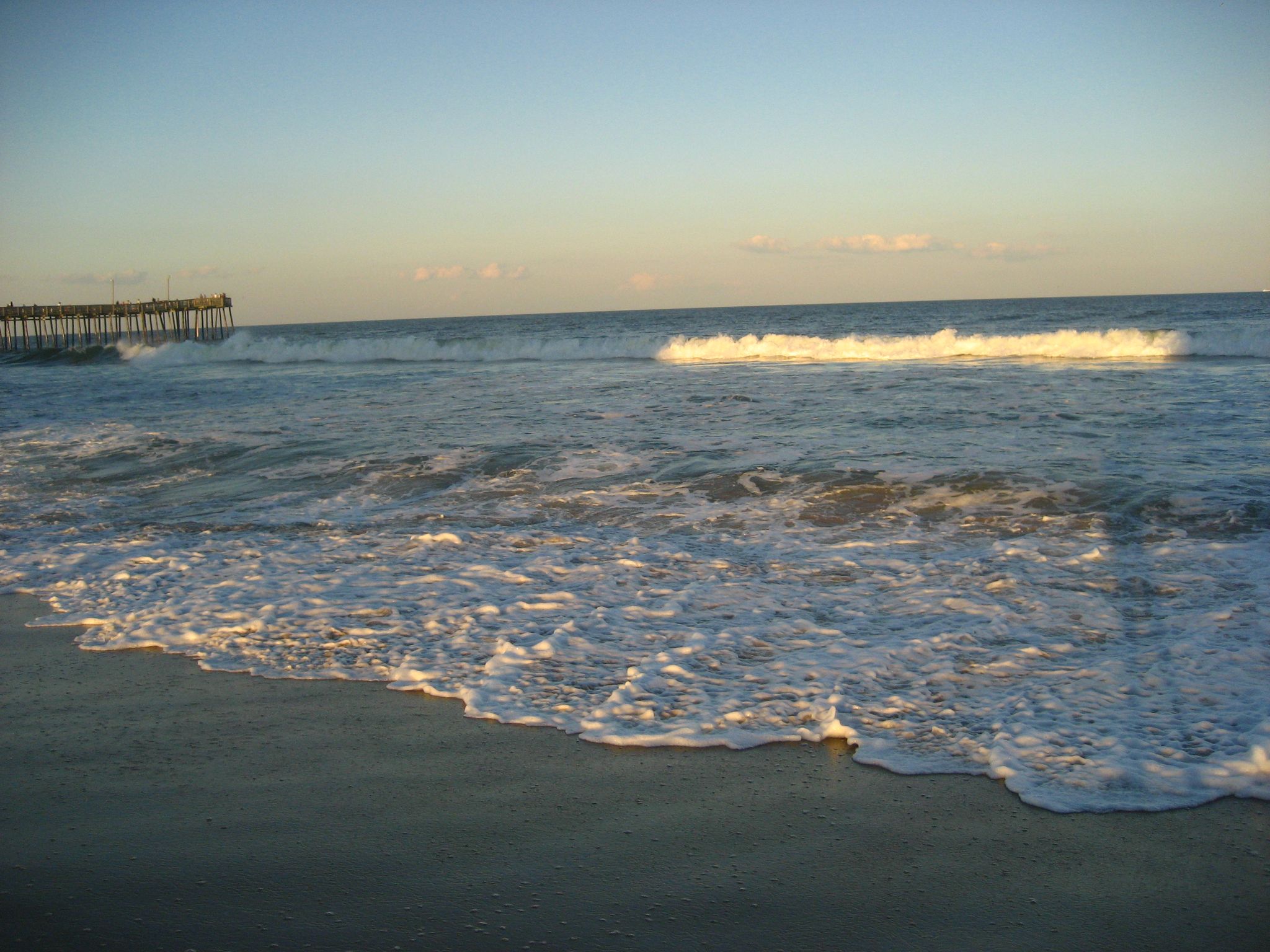 Ocean waves break on a sandy shore, a pier visible in the distance. - Virginia Beach and First Landing State Park loop