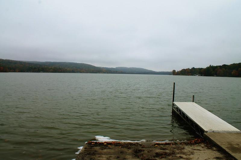 Overcast day over a calm lake with a wooden dock and distant hills.