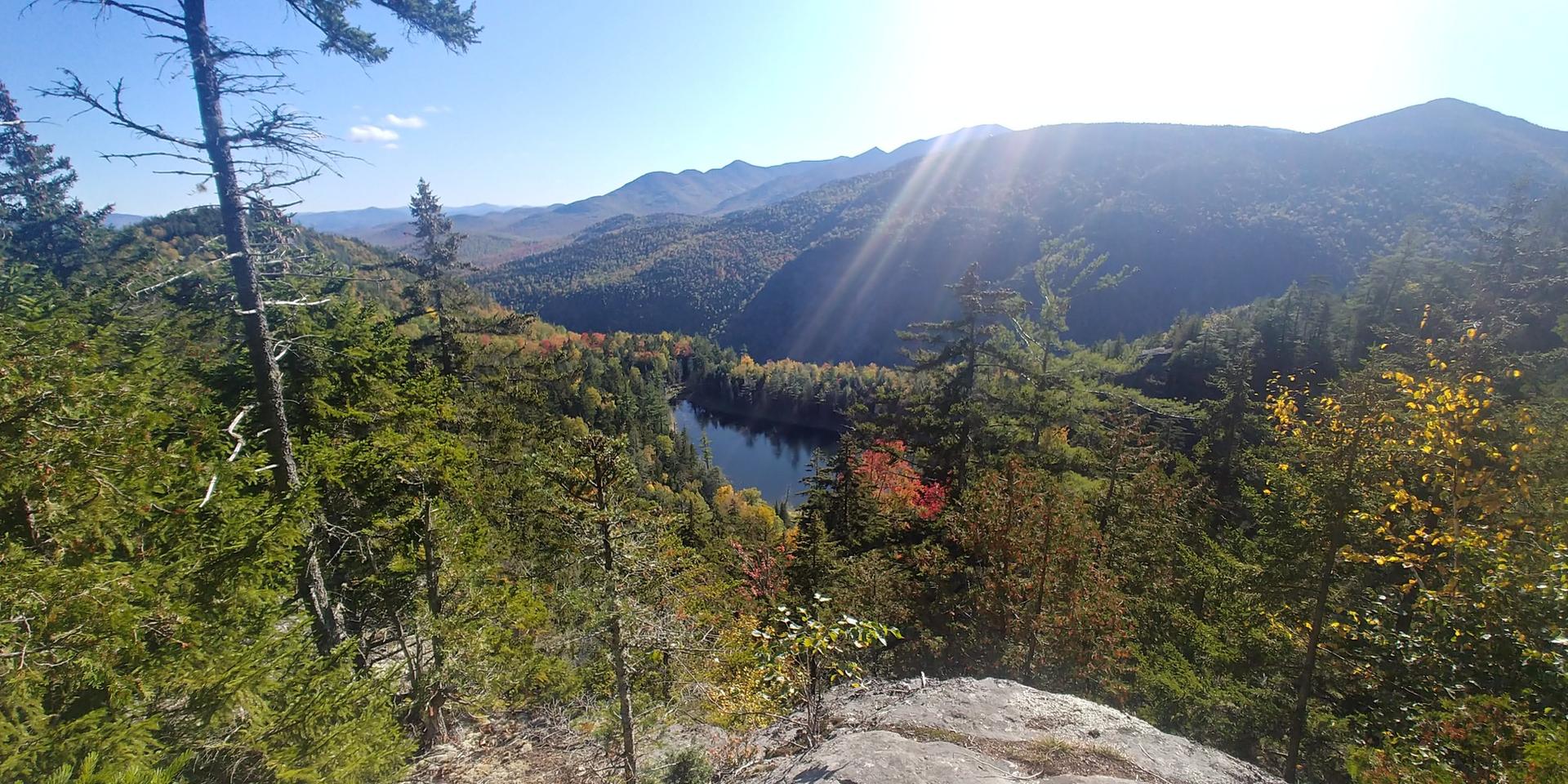 Sunny mountain view overlooking a lake surrounded by vibrant autumn trees.