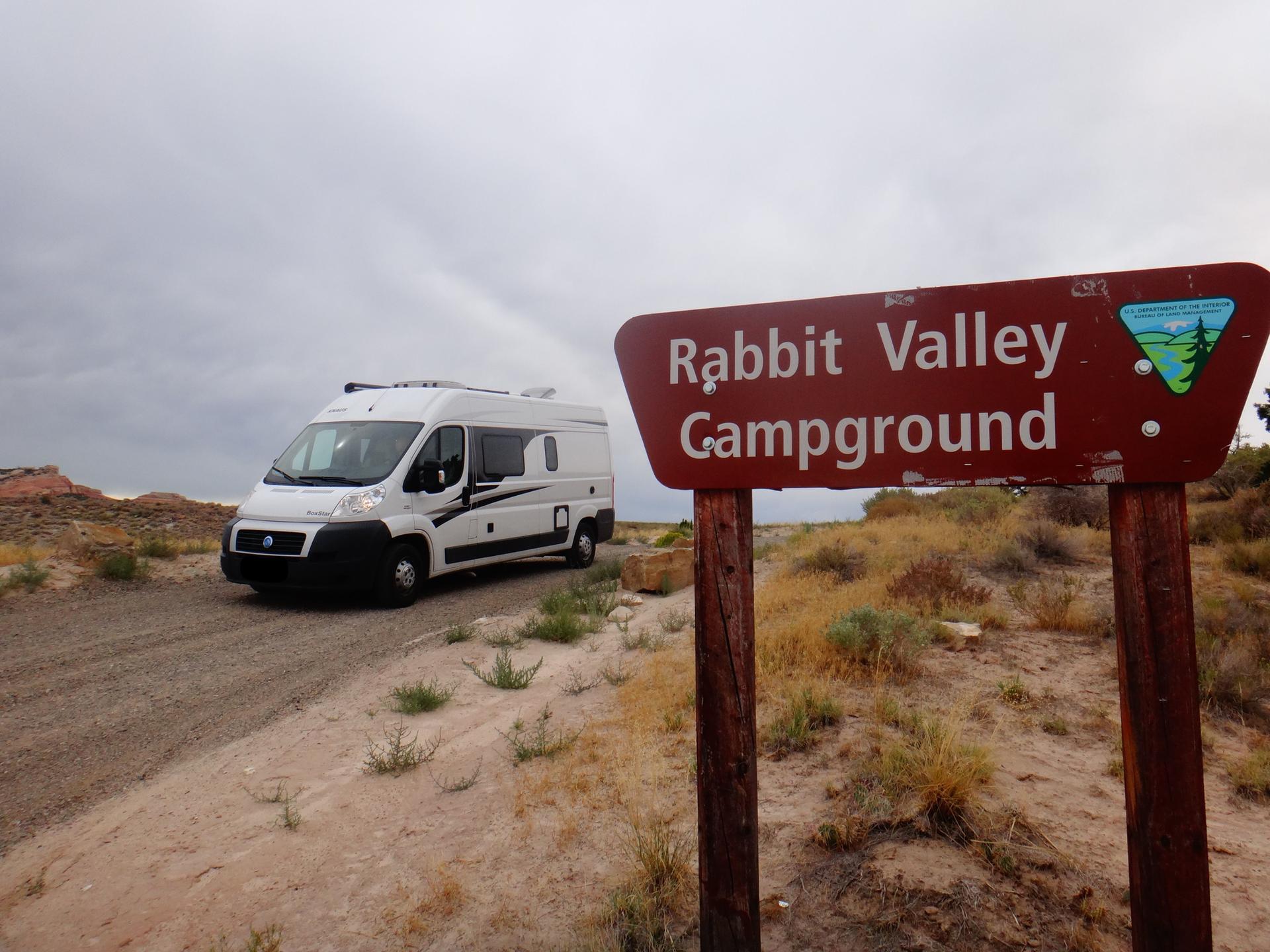 A white camper van on a dirt road next to a campground sign.