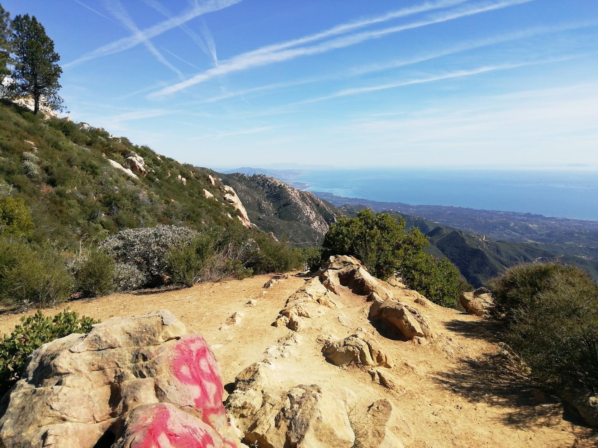Sunny dirt path with painted rocks overlooking mountains and distant ocean.