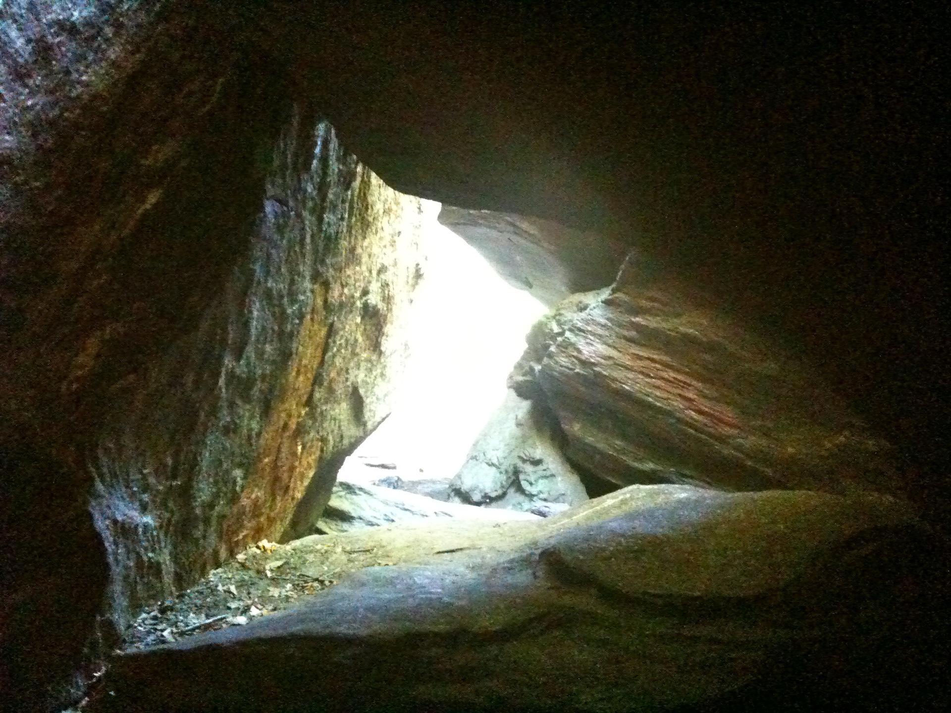 Rocky cave interior with a bright, triangular exit to daylight.