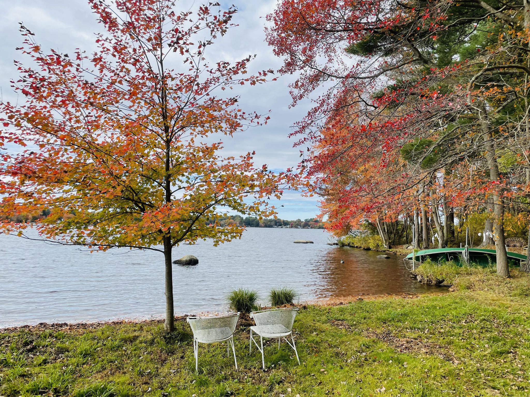 Autumn trees with red and orange leaves frame a lake with two empty chairs. - Peace in the Woods – Big River State Management Area