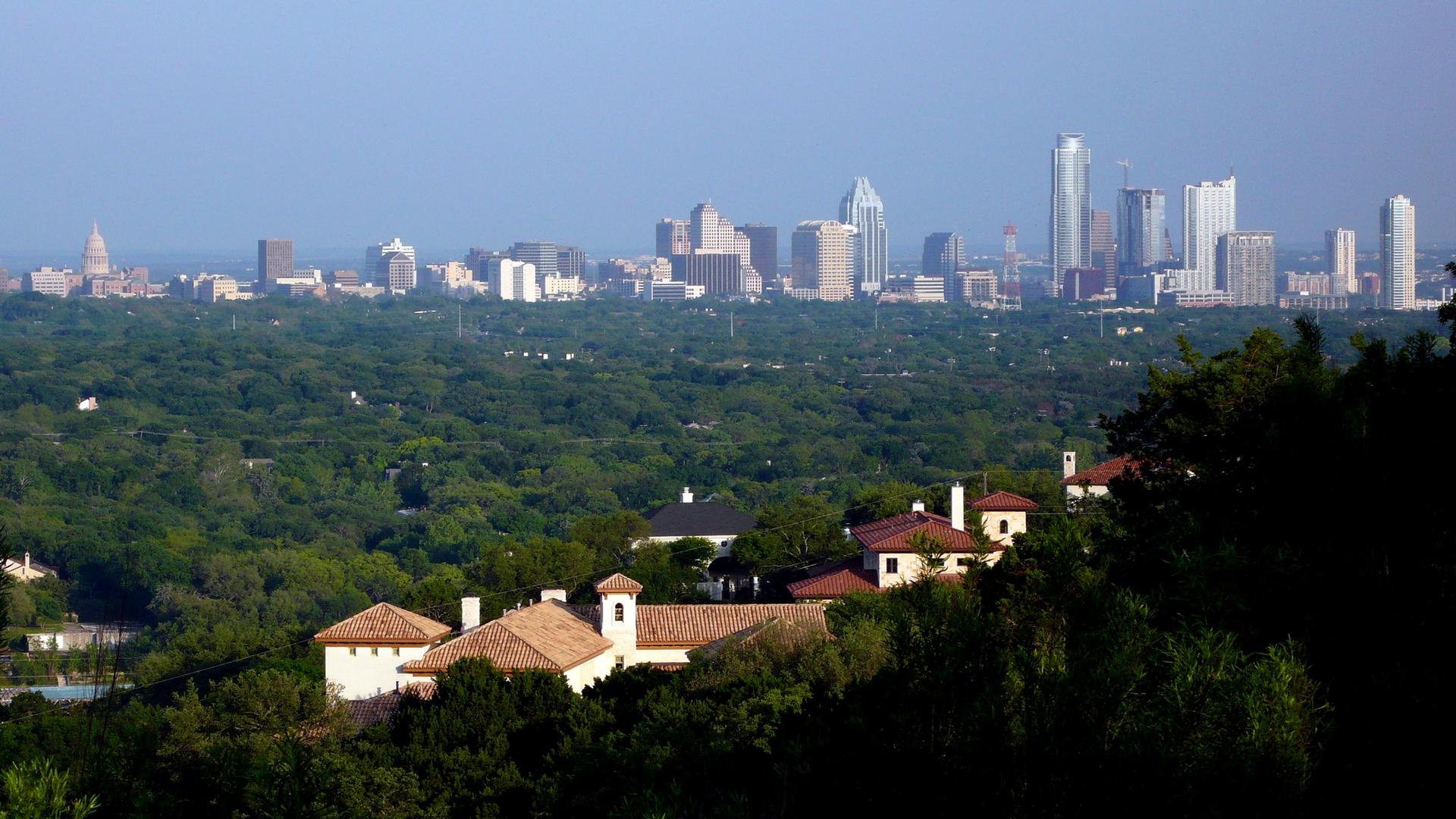 City skyline above a dense green forest and residential area on a clear day.
