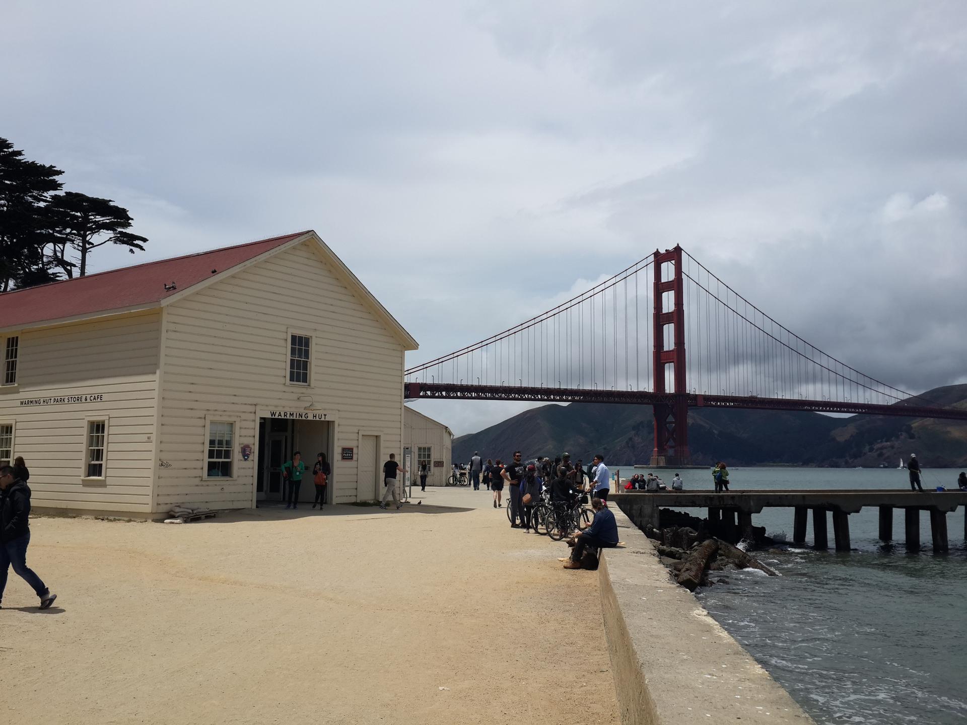 White building and red bridge under cloudy sky, people on waterfront.