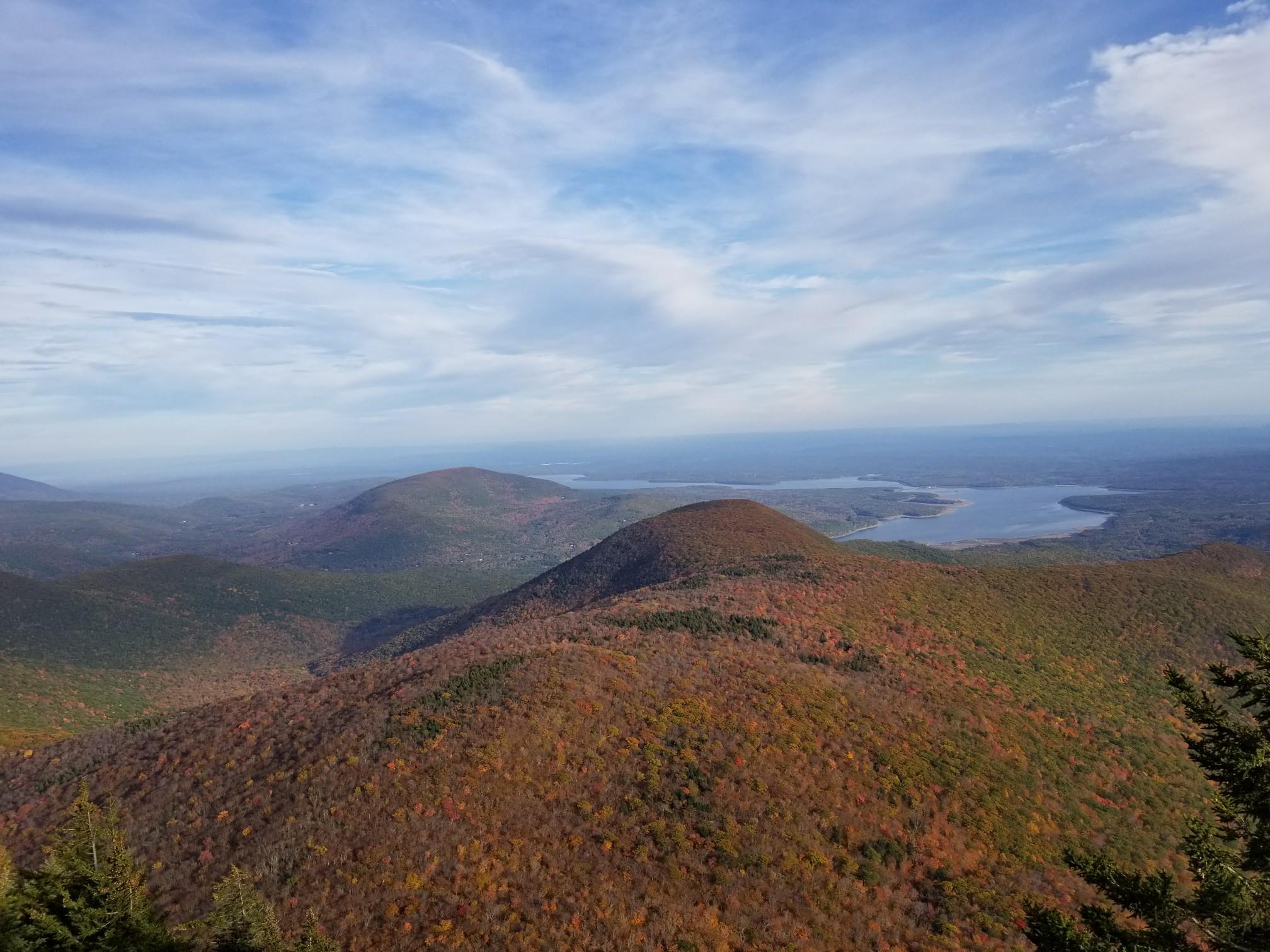 Autumn hills with a distant lake under a bright blue and cloudy sky.