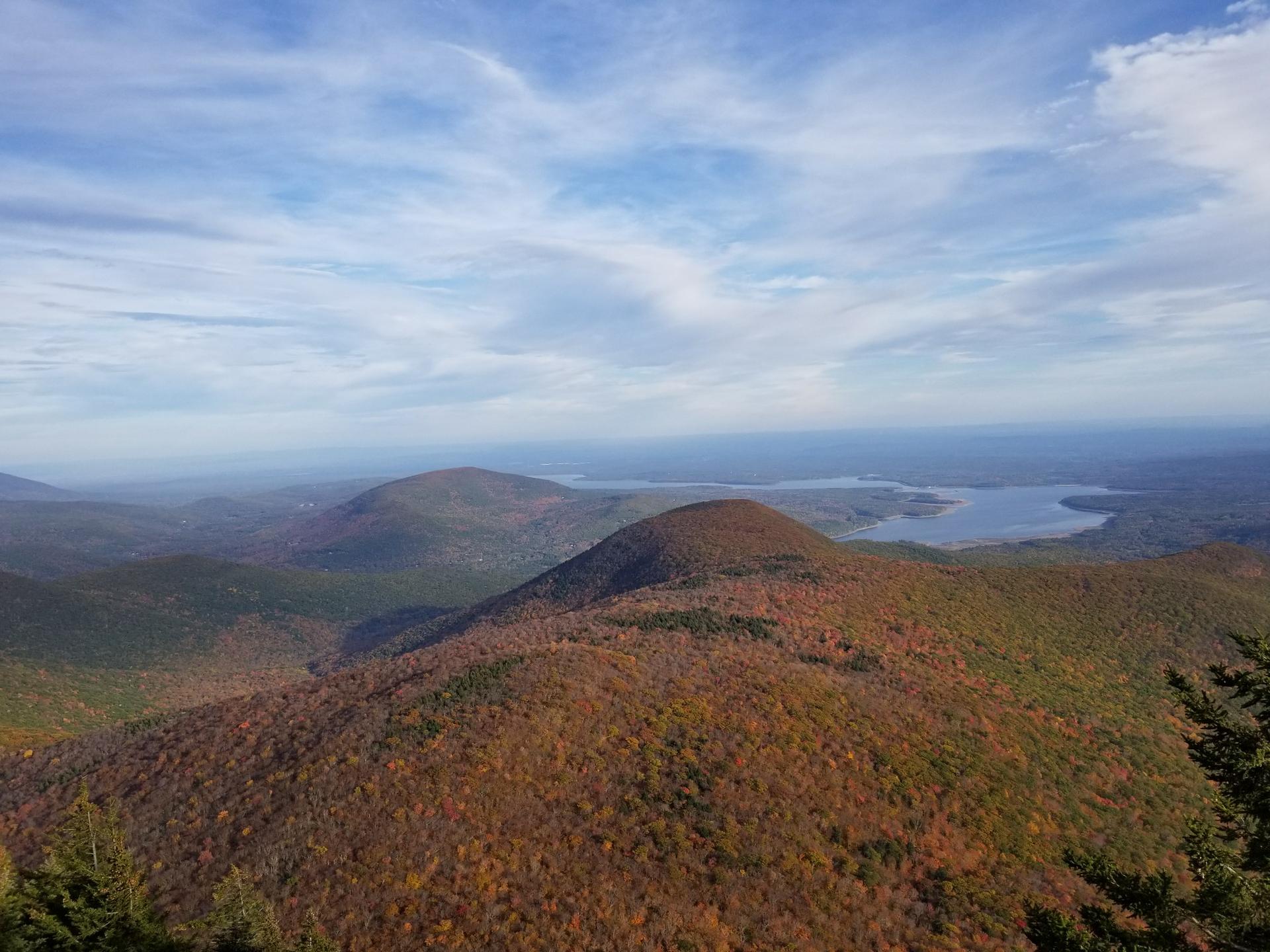 Autumn hills with a distant lake under a bright blue and cloudy sky.