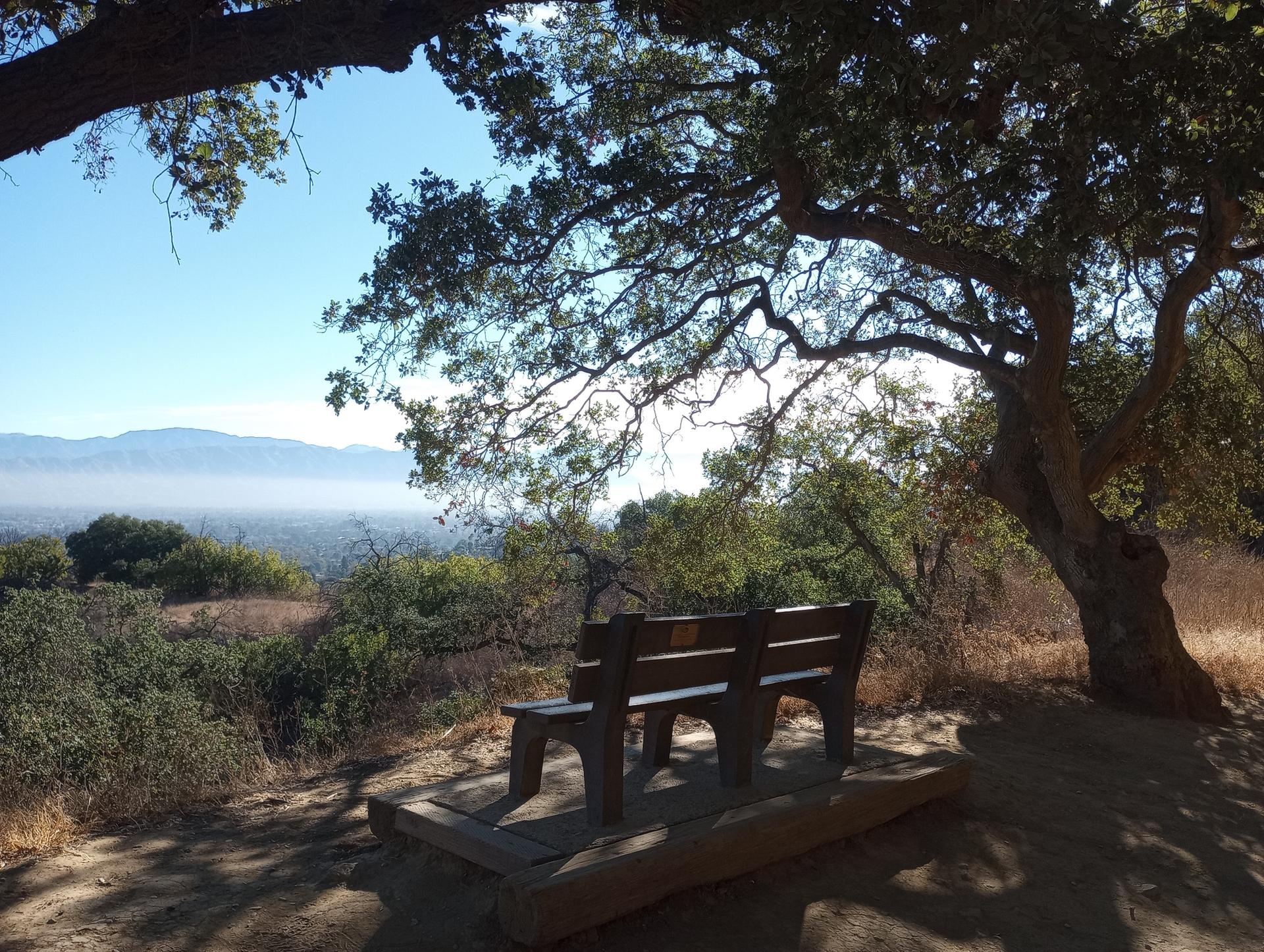 Shaded wooden bench overlooking a hazy valley and distant mountains.