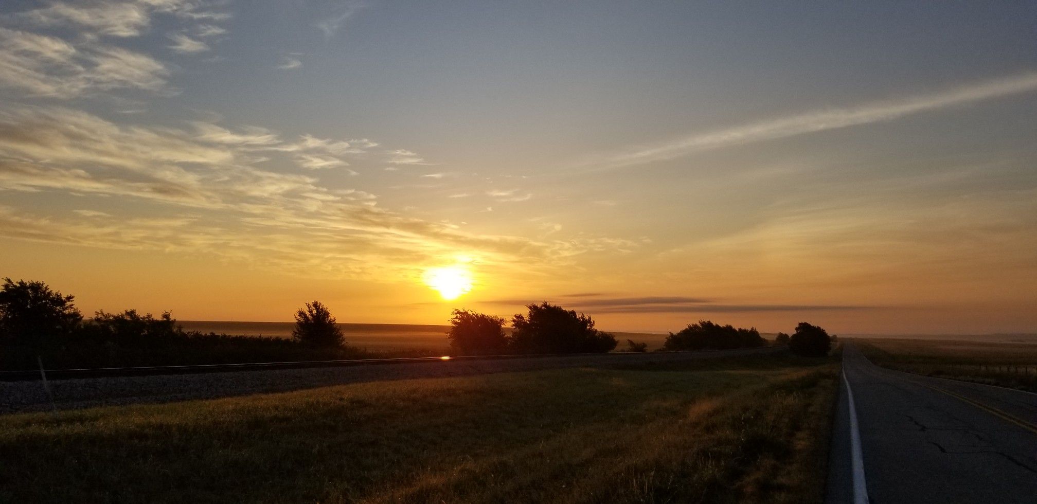 Golden sunrise over a rural road and field with distant trees. - Forth Worth and Benbrook loop