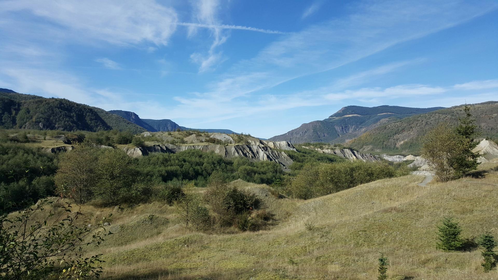 Green valley with eroded hills and distant mountains under a blue sky.