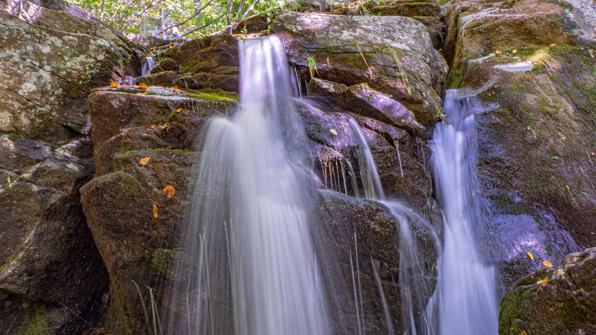 Long exposure of a multi-tiered waterfall cascading over mossy rocks.