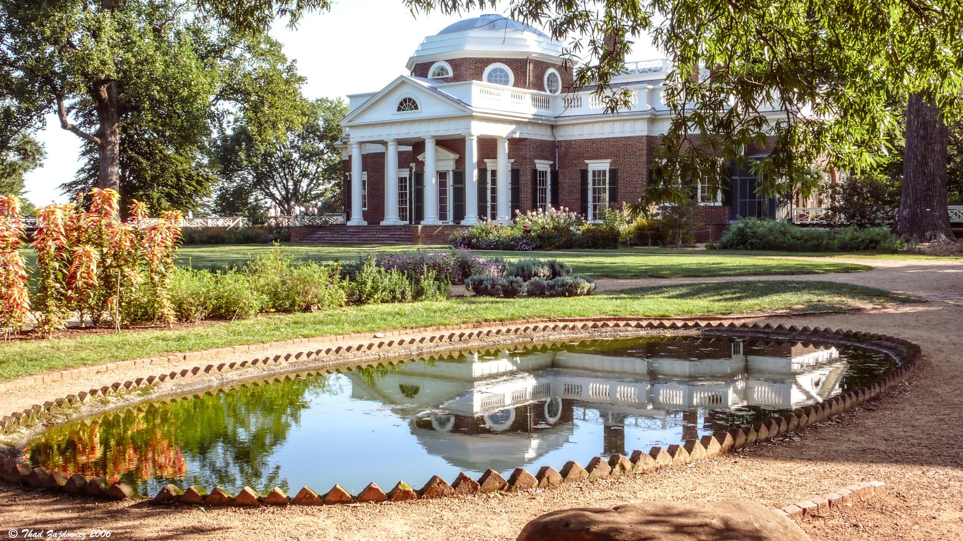 Grand building with columns reflected in a calm pond on a sunny day.