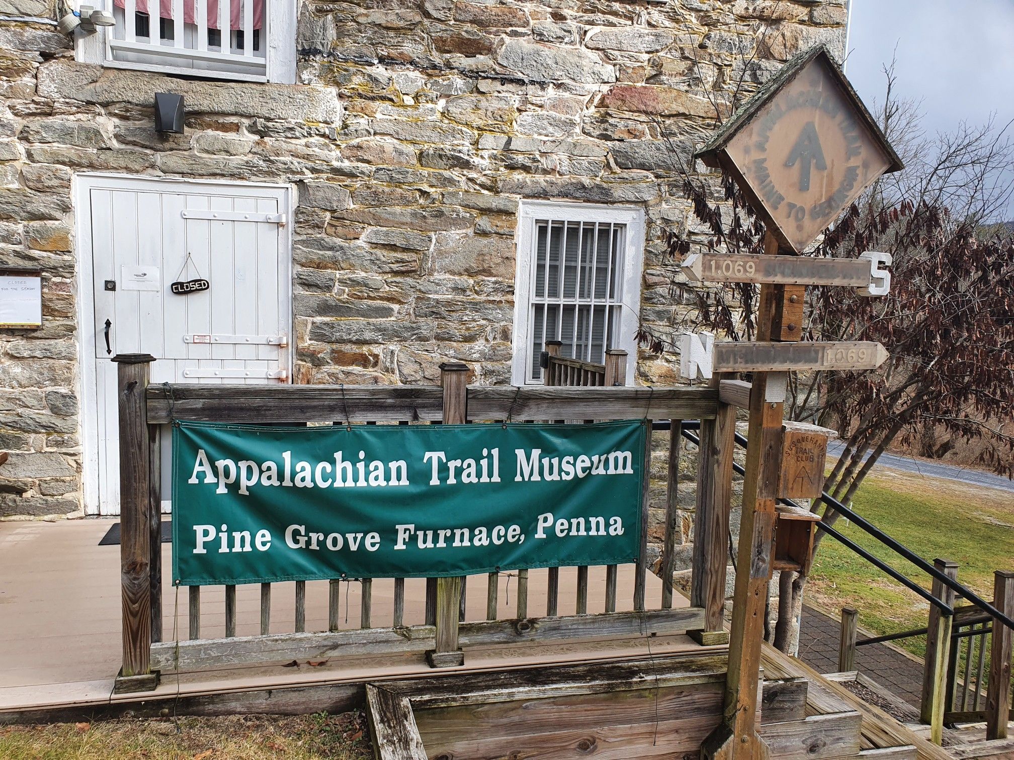 A stone building with a white door and a green banner on a wooden railing. - Sunset Rocks and Appalachian Trail Loop
