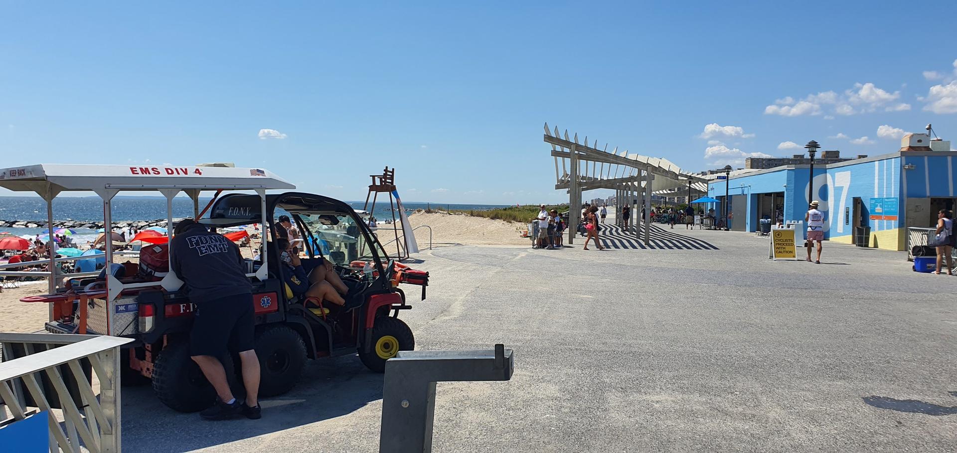 Lifeguard vehicle on a sunny boardwalk next to a busy beach.