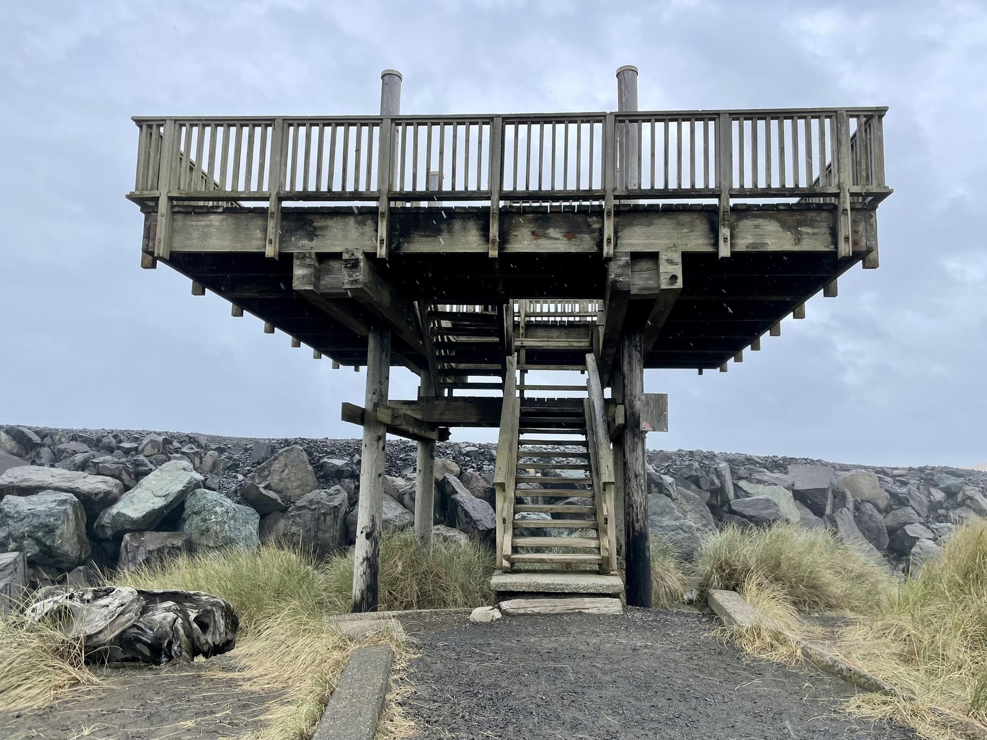 A wooden observation deck with stairs overlooks a rocky jetty.