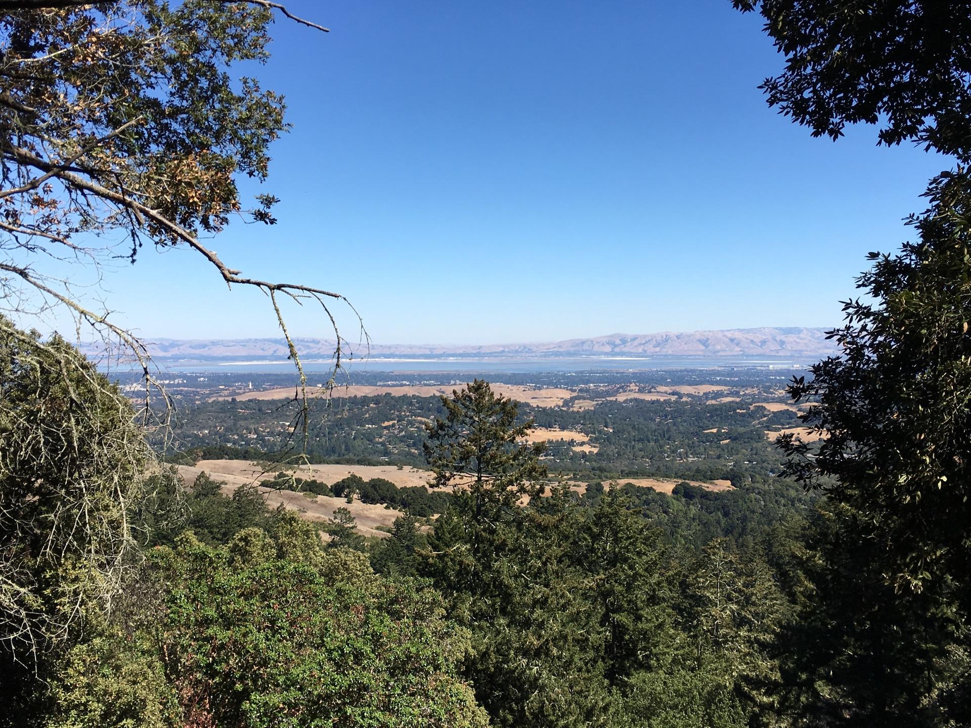 Vast valley view with forests, fields, and distant mountains under a clear blue sky.